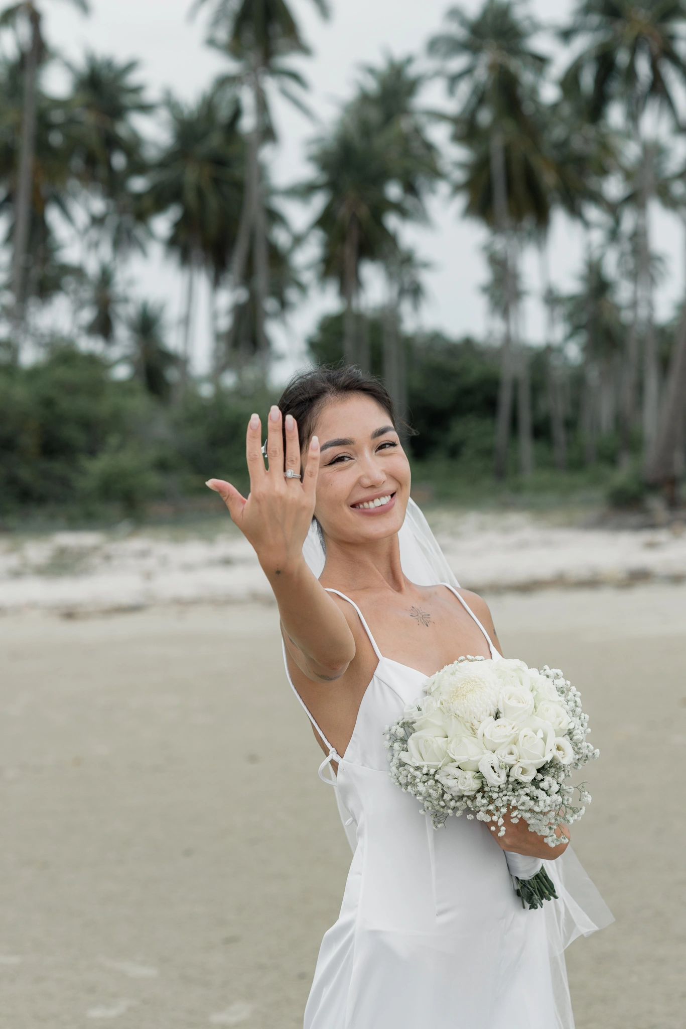Bride smiling and showing her ring on the beach