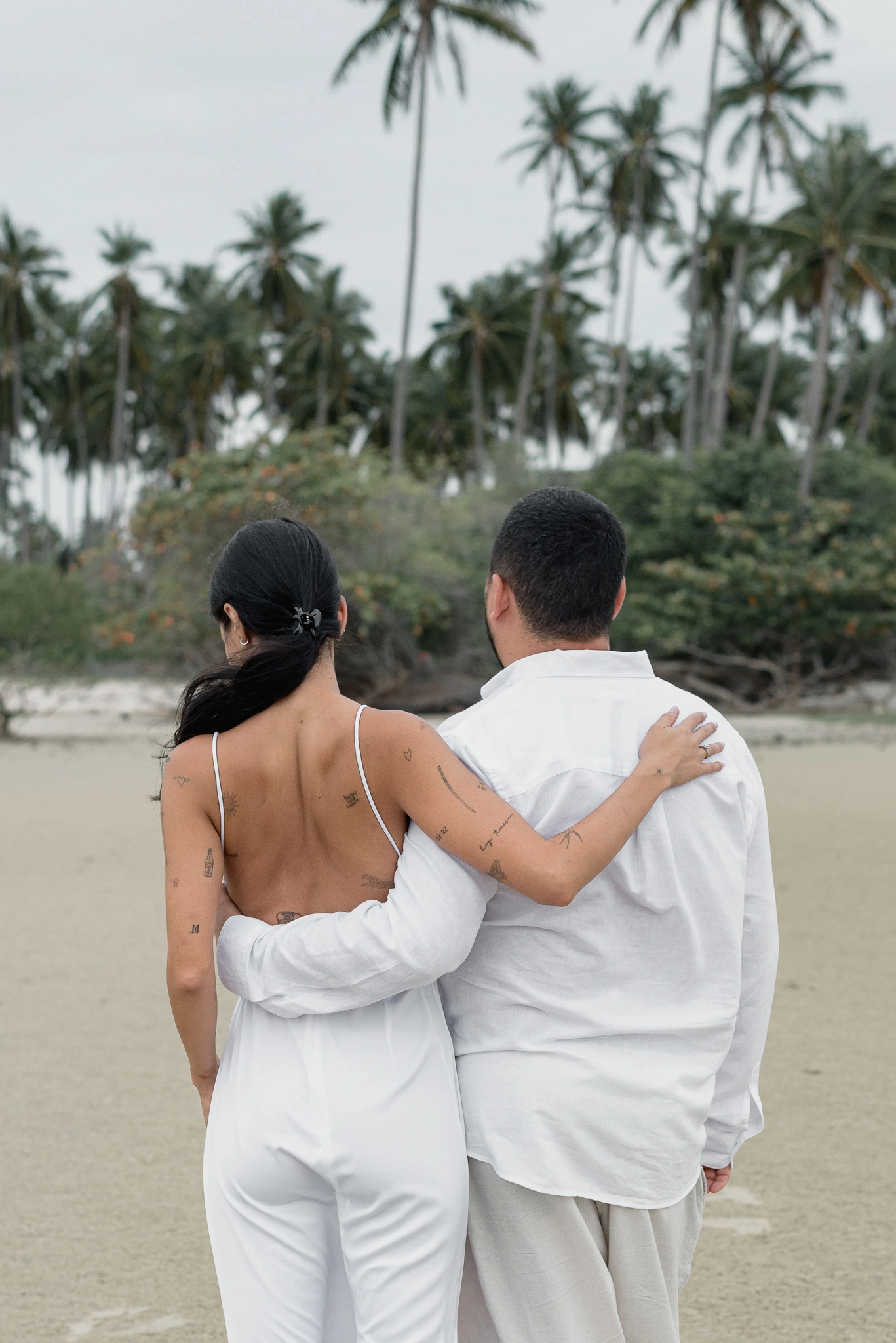 Couple embracing from behind beneath palm trees
